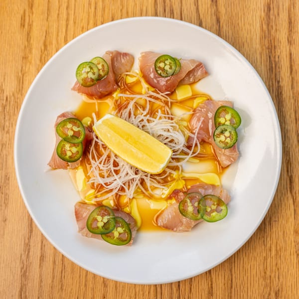 Restaurant Tatsuki's yellowtail sashimi with jalapeños, shredded daikon, and a lemon wedge on a white plate.