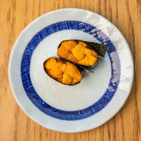 Two pieces of bright orange uni (sea urchin) sushi wrapped in nori on a white and blue plate.