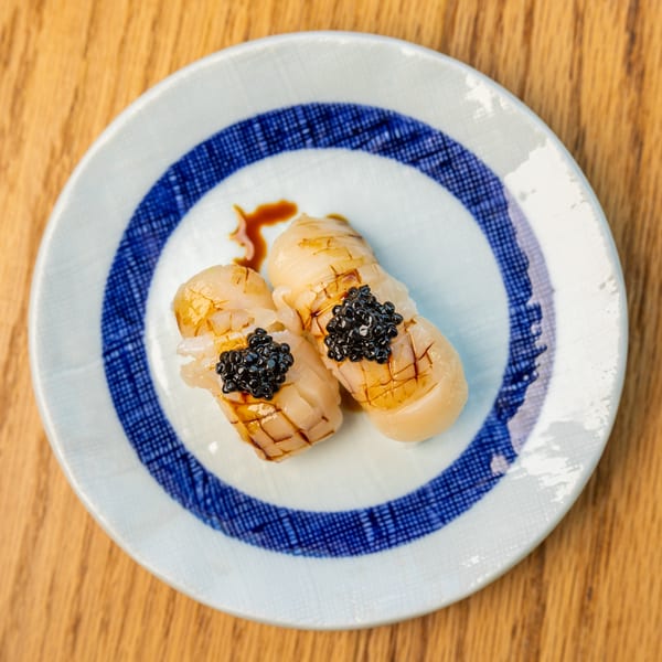 Two pieces of seared scallop nigiri sushi topped with black caviar on a patterned plate.